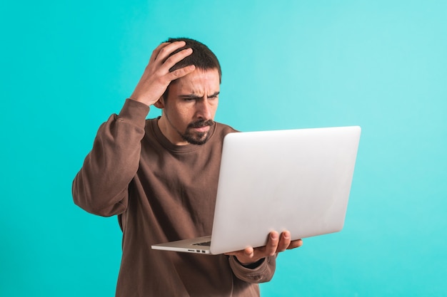 Young handsome man isolated over blue background using his laptop computer working Copy space text