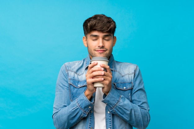 Giovane uomo bello sopra il caffè blu isolato della tenuta della parete da portare via