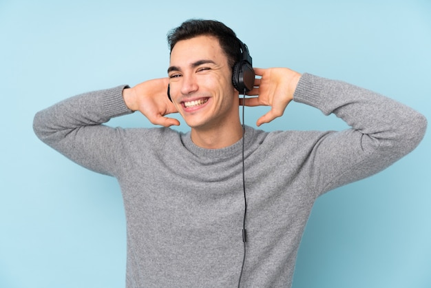 Young handsome man isolated on blue wall listening music