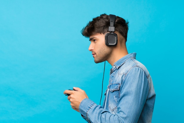 ビデオゲームで遊ぶ孤立した青い壁の上の若いハンサムな男