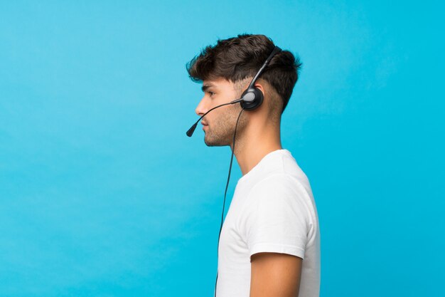 Young handsome man over isolated blue  working with headset