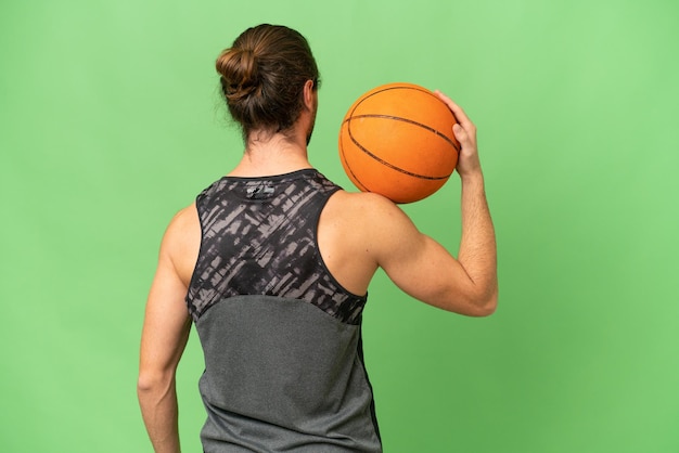 Giovane uomo bello isolato su sfondo verde croma che gioca a basket in posizione posteriore