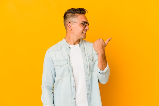 Young handsome man isolated points with thumb finger away, laughing and carefree