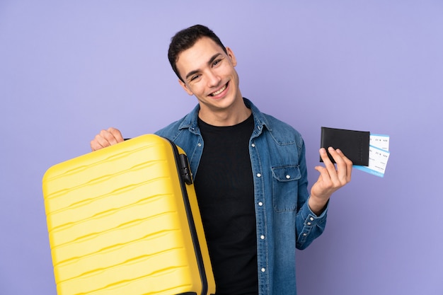 Young handsome man isolated on purple wall in vacation with suitcase and passport