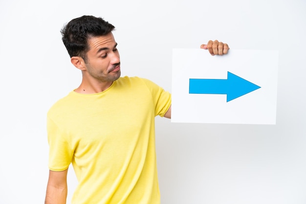 Photo young handsome man over isolated white background holding a placard with arrow symbol