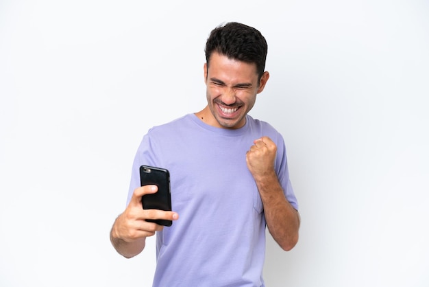 Young handsome man over isolated white background using mobile phone and doing victory gesture