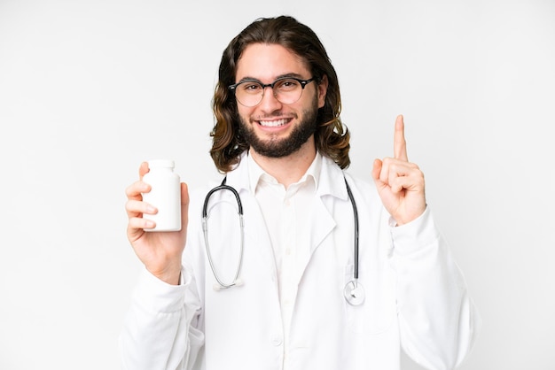 Young handsome man over isolated white background wearing a doctor gown and holding pills