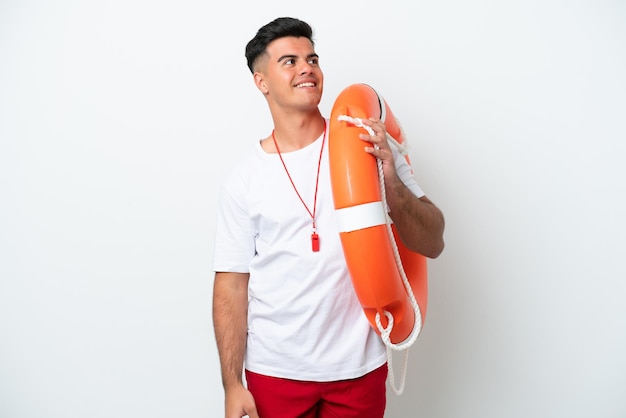 Young handsome man isolated on white background with lifeguard equipment and looking up while smiling