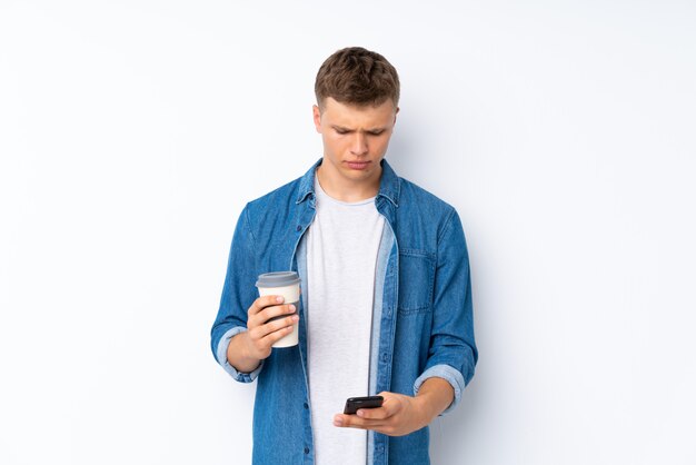 Young handsome man over isolated white holding coffee to take away and a mobile