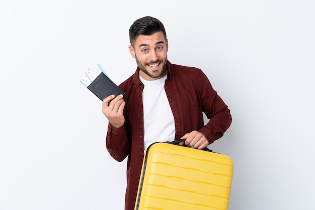 Young handsome man over isolated white wall in vacation with suitcase and passport