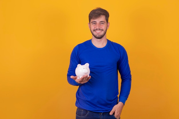 Young handsome man over isolated yellow background holding a big piggybank