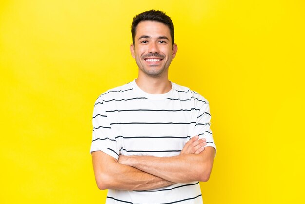 Young handsome man over isolated yellow background keeping the arms crossed in frontal position