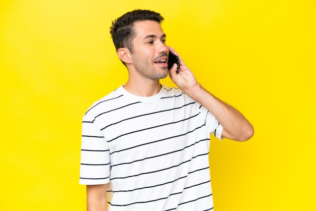 Young handsome man over isolated yellow background keeping a conversation with the mobile phone