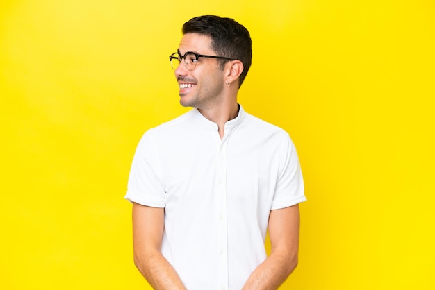 Young handsome man over isolated yellow background looking to the side and smiling