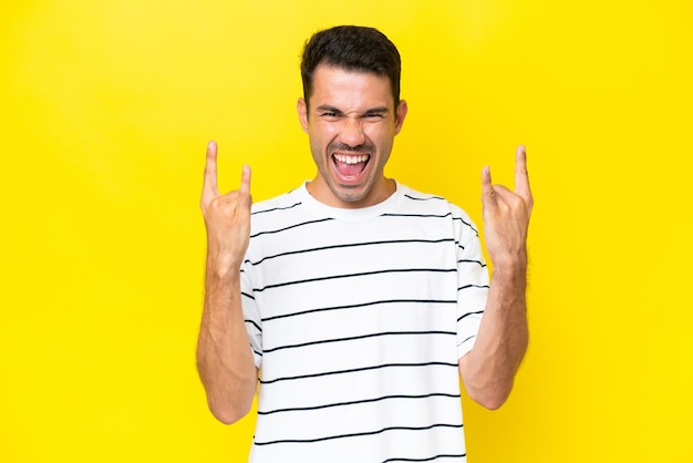 Young handsome man over isolated yellow background making horn gesture