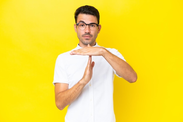 Young handsome man over isolated yellow background making time out gesture