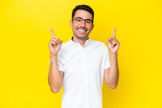 Young handsome man over isolated yellow background pointing up a great idea