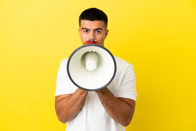 Foto giovane uomo bello su sfondo giallo isolato che grida attraverso un megafono per annunciare qualcosa