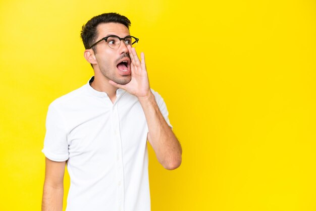 Young handsome man over isolated yellow background shouting with mouth wide open to the side