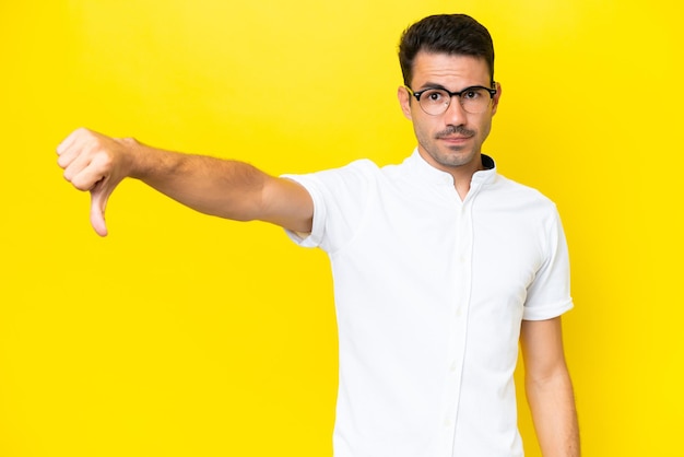 Young handsome man over isolated yellow background showing thumb down with negative expression