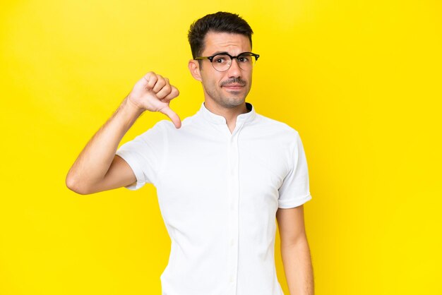 Young handsome man over isolated yellow background showing thumb down with negative expression