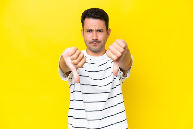 Young handsome man over isolated yellow background showing thumb down with two hands