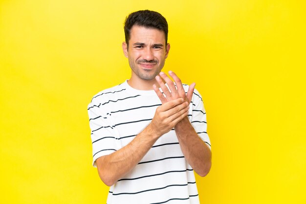 Young handsome man over isolated yellow background suffering from pain in hands