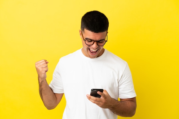 Young handsome man over isolated yellow background surprised and sending a message