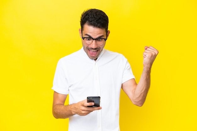 Young handsome man over isolated yellow background surprised and sending a message