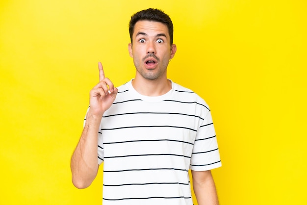 Young handsome man over isolated yellow background thinking an idea pointing the finger up