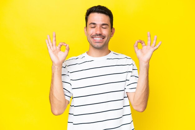 Young handsome man over isolated yellow background in zen pose