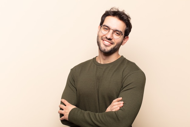 Young handsome man laughing happily with arms crossed, with a relaxed, positive and satisfied pose