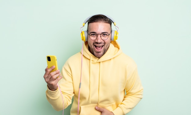 Young handsome man laughing out loud at some hilarious joke. headphones and smartphone concept