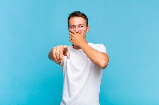 Young handsome man laughing at you, pointing to camera and making fun of or mocking you