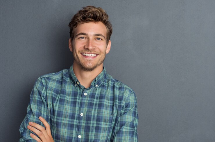 Photo young handsome man leaning against grey wall with arms crossed