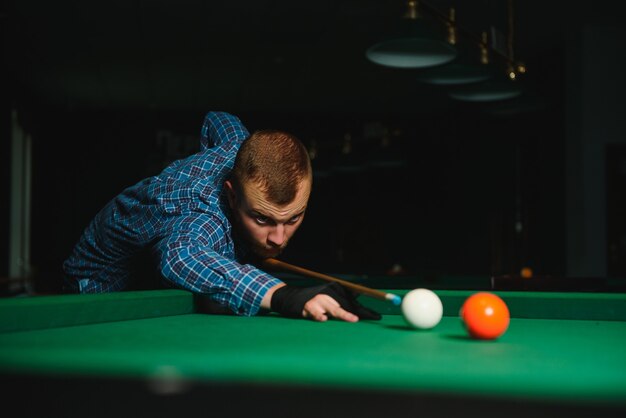 Young handsome man leaning over the table while playing snooker