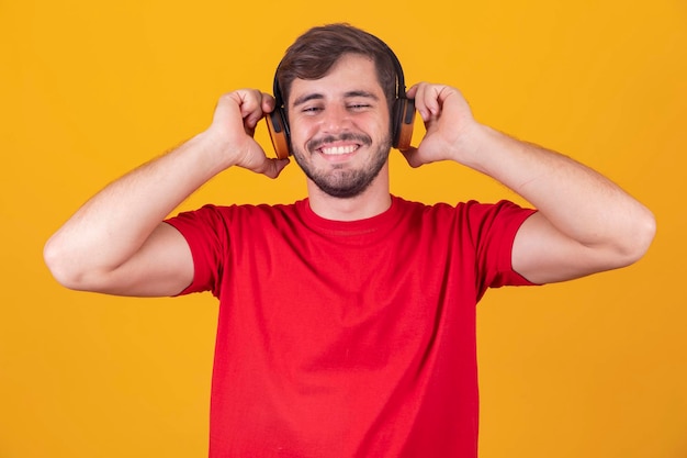 Young handsome man listening to music on headphones yellow studio background isolated smiling happy