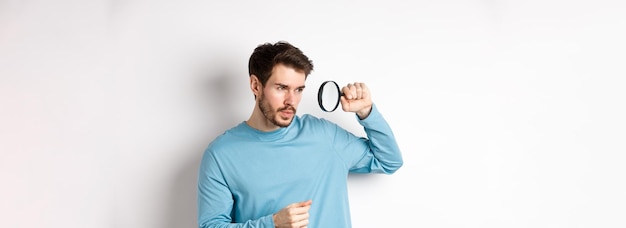 Photo young handsome man look through magnifying glass with curious face investigating or searching for         person