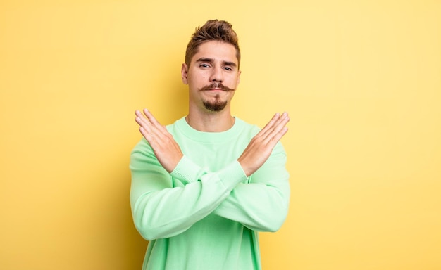 Young handsome man looking annoyed and sick of your attitude saying enough hands crossed up front telling you to stop strange moustache concept