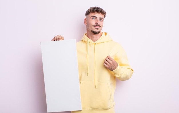 Photo young handsome man looking arrogant, successful, positive and proud. blank canvas concept