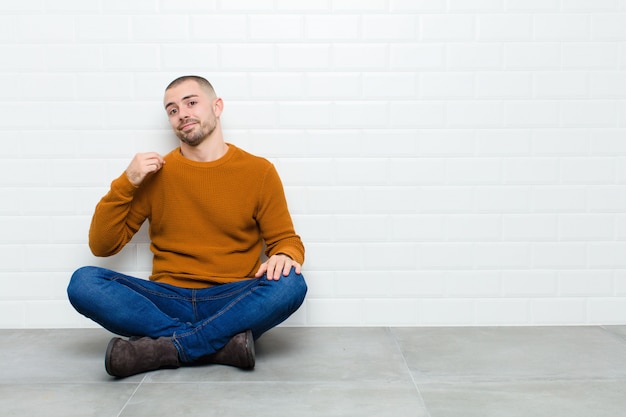 Foto giovane uomo bello che sembra arrogante, di successo, positivo e orgoglioso, indicando se stesso seduto sul pavimento