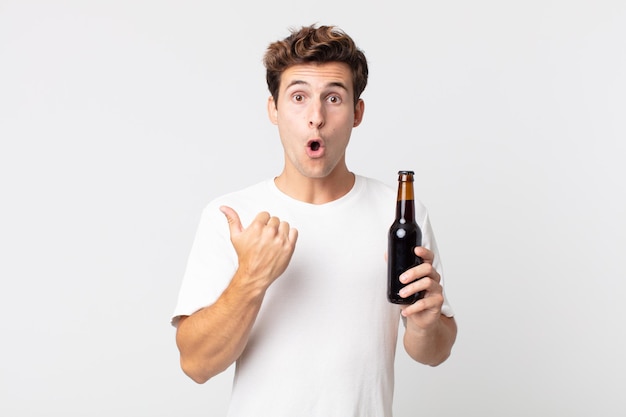 Young handsome man looking astonished in disbelief and holding a beer bottle