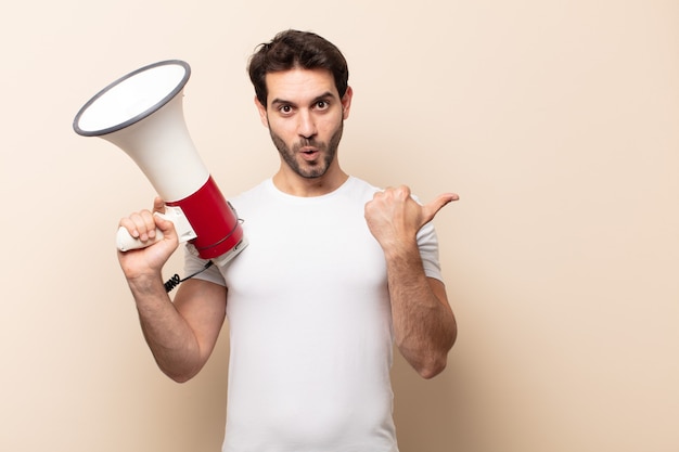 Young handsome man looking astonished in disbelief, pointing at object on the side and saying wow, unbelievable