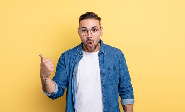 Young handsome man looking astonished in disbelief, pointing at object on the side and saying wow, unbelievable