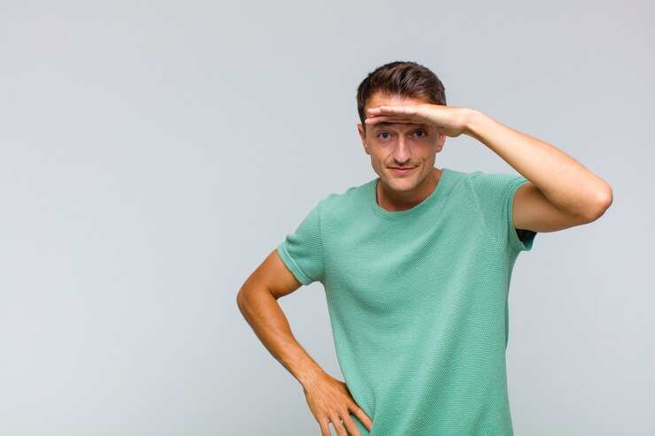 Photo young handsome man looking bewildered and astonished, with hand over forehead looking far away, watching or searching