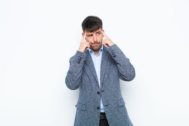 Young handsome man looking concentrated and thinking hard on an idea, imagining a solution to a challenge or problem on white wall