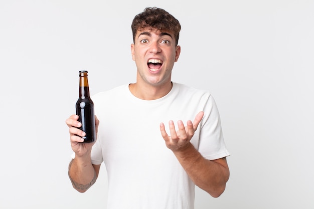 Young handsome man looking desperate, frustrated and stressed and holding a beer bottle