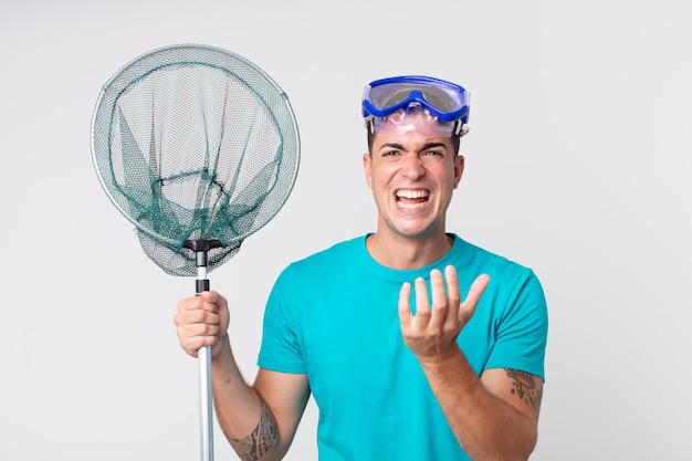 Young handsome man looking desperate, frustrated and stressed with goggles and fishing net