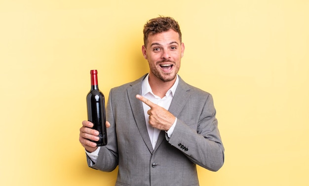 Young handsome man looking excited and surprised pointing to the side. bottle of wine concept