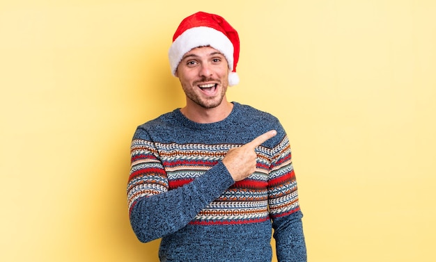 Young handsome man looking excited and surprised pointing to the side christmas concept